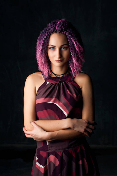 young beautiful girl with pink curly hair in purple dress on a dark background - Φωτογραφία, εικόνα