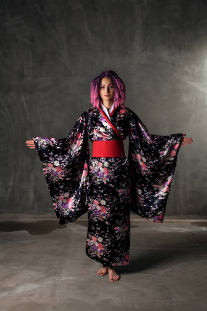 young girl with pink, curly hair in a colored kimono on a black background - Foto, Imagen