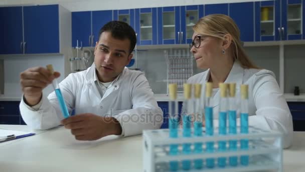 Chemists analyzing test tubes with liquid in lab - Materiał filmowy, wideo