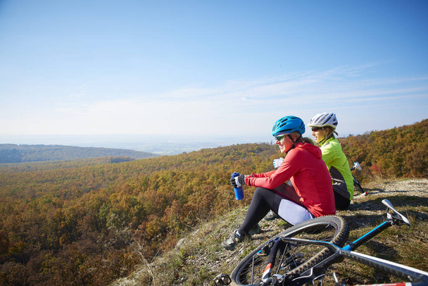Full length shot of two female cyclist relaxing on the rock of the top of the mountain. - Fotoğraf, Görsel