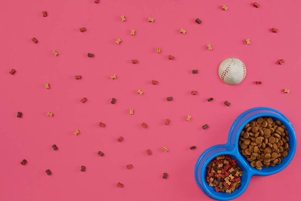 Droog voedsel voor huisdieren in kom met een bal op roze achtergrond bovenaanzicht - Foto, afbeelding