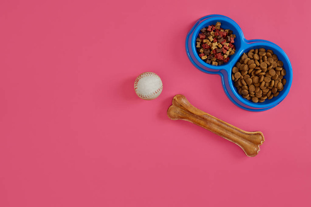 Nourriture sèche pour animaux de compagnie dans un bol avec une balle et un os de chien sur fond rose vue de dessus
 - Photo, image