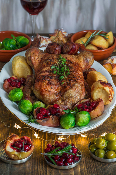 Pato asado festivo en mesa de madera con brotes de Bruselas, papas al horno, manzanas y salsa de arándanos
 - Foto, imagen