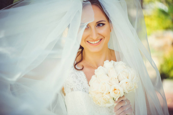 ihale mutlu gelin peçe, mutlu kadınla ellerini, buket düğün elbise içinde beyaz peçe yüz, yumuşak ve sıcak kapsar. - Fotoğraf, Görsel
