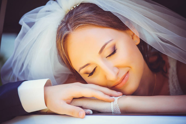 zarte glückliche Braut im Auto, eine glückliche Frau im Hochzeitskleid legt ihren Kopf auf den Arm der Moschchina, weißer Schleier auf ihren Kopf - Foto, Bild
