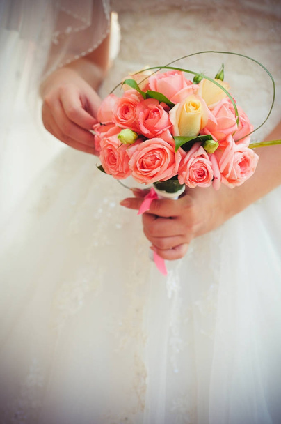 El ramo rosado de boda de las rosas en las manos de la novia en el vestido blanco, la tonificación tierna caliente
 - Foto, Imagen