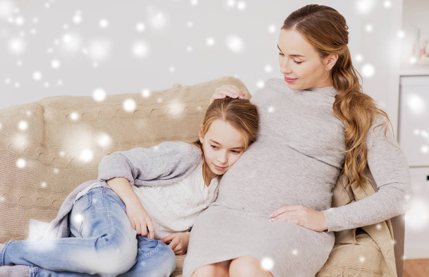 happy pregnant woman and girl on sofa at home - Foto, Imagen
