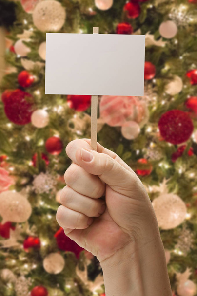 Kezében díszített karácsonyfa előtt üres kártya. - Fotó, kép