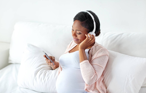 pregnant woman in headphones with smartphone - Foto, Imagen