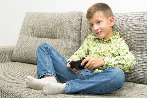 Boy playing video games with joystic sitting on sofa - Photo, image