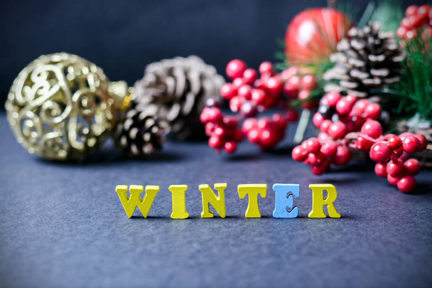 Η λέξη - χειμερινό κίτρινο ξύλινες επιστολές σε γκρι φόντο με δώρα, Χριστουγεννιάτικα διακοσμητικά, κουκουνάρια και ένα εορταστικό στεφάνι. έννοια του νέου έτους. - Φωτογραφία, εικόνα