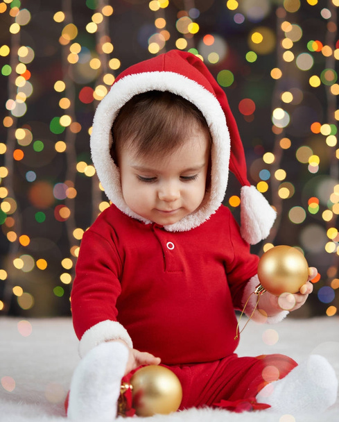 little kid boy dressed as santa playing with christmas toys, dark background with illumination, happy new year and winter holiday concept - Φωτογραφία, εικόνα