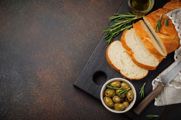 Italian traditional Ciabatta bread with olives, olive oil, pepper and rosemary on a dark stone or concrete background.  - Foto, imagen