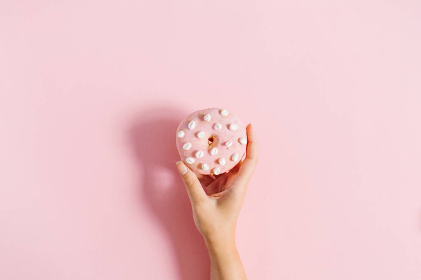 Women's hand holding donut on pink background. Minimal flat lay, top view concept. - Foto, Imagem