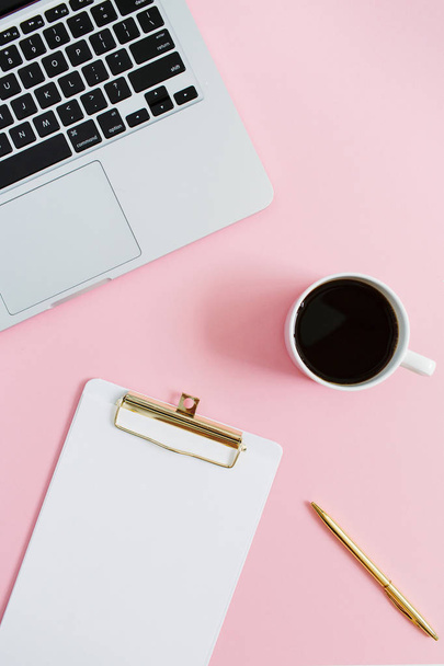 Minimale vrouwen home office-bureaublad met laptop, klembord, pen, koffiemok op roze achtergrond. Plat lag, top uitzicht werkruimte concept. - Foto, afbeelding