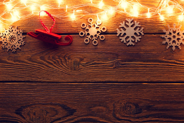 Picture of wooden surface with burning garland on top, snowflakes, red felt toy. - Fotoğraf, Görsel