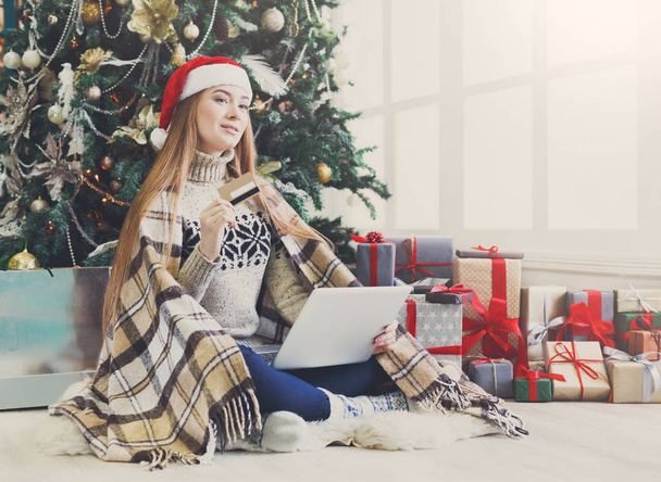 Молода жінка купує онлайн в затишному різдвяному інтер'єрі
 - Фото, зображення