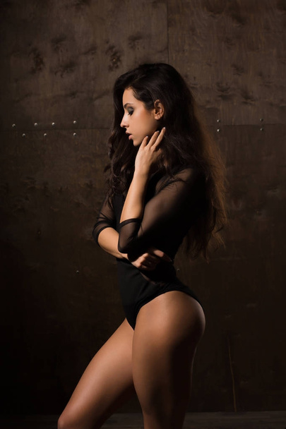 Attractive tanned young woman with lush hair in black lingerie p - 写真・画像