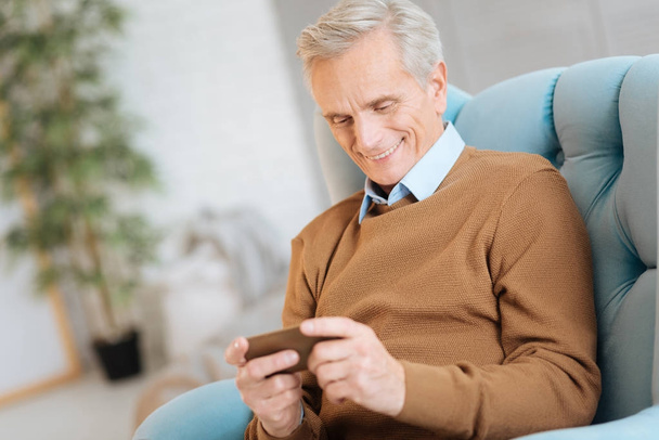 Smiling retired gentleman reading news on phone - Фото, изображение