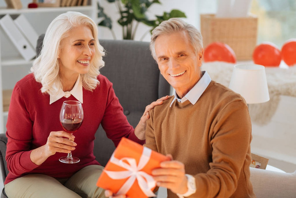 Adorable retired couple exchanging gift during anniversary celebration - Foto, imagen