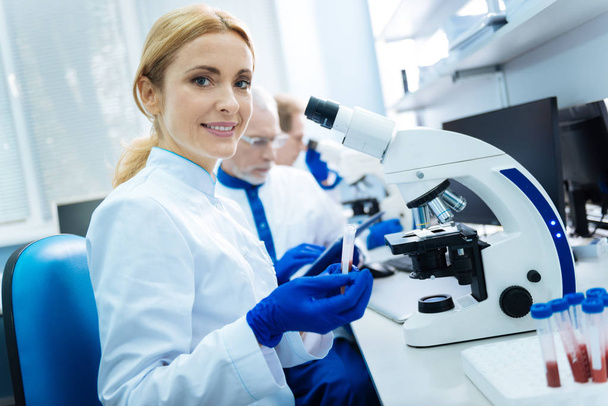 Smiling scientist sitting at a microscope - Zdjęcie, obraz