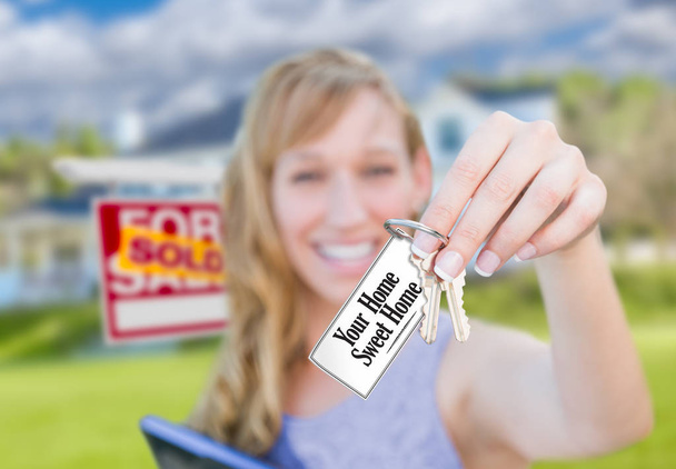 Woman Holding New House Keys with Your Home Sweet Home Card In Front of Sold Real Estate Sign and Home. - Photo, Image