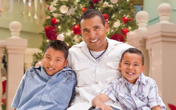 Ισπανόφωνος νέος πατέρας και γιοι μπροστά από το στολισμένο χριστουγεννιάτικο δέντρο. - Φωτογραφία, εικόνα
