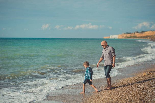 Dad and son walking along the seashore. Dad and son walking along the shore of the ocean. Weekend at the beach. A beach Stone. A sea foam. - Foto, immagini