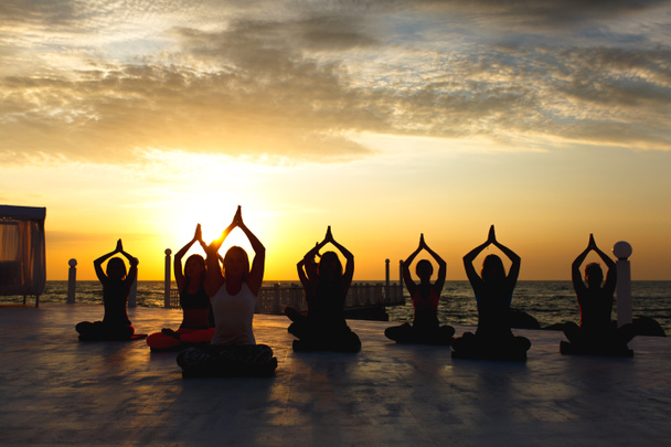 A group of women doing yoga at sunrise near the sea - Photo, Image
