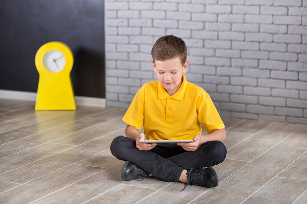 Cute handsome school boy in yellow t-shirt tie and stylish boots casuals standing cloase to black board with numbers and holding tablet and smiling - Zdjęcie, obraz