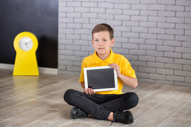 Cute handsome school boy in yellow t-shirt tie and stylish boots casuals standing cloase to black board with numbers and holding tablet and smiling - Fotó, kép