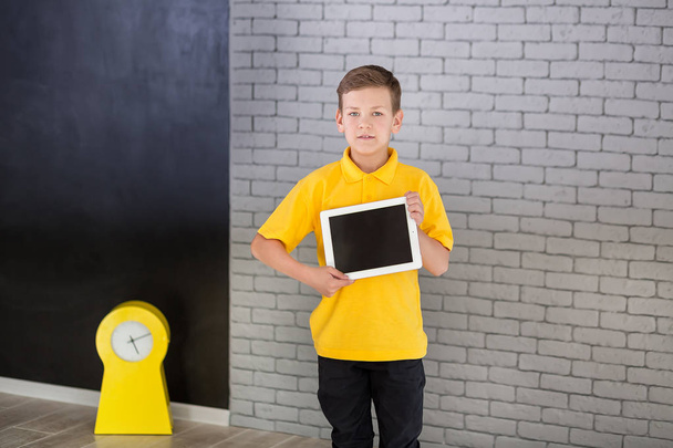 Cute handsome school boy in yellow t-shirt tie and stylish boots casuals standing cloase to black board with numbers and holding tablet and smiling - Fotó, kép