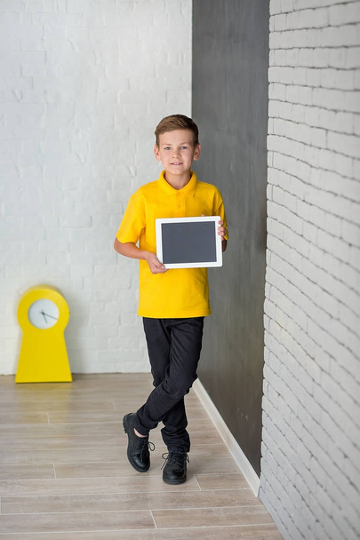 Cute handsome school boy in yellow t-shirt tie and stylish boots casuals standing cloase to black board with numbers and holding tablet and smiling - Foto, Bild