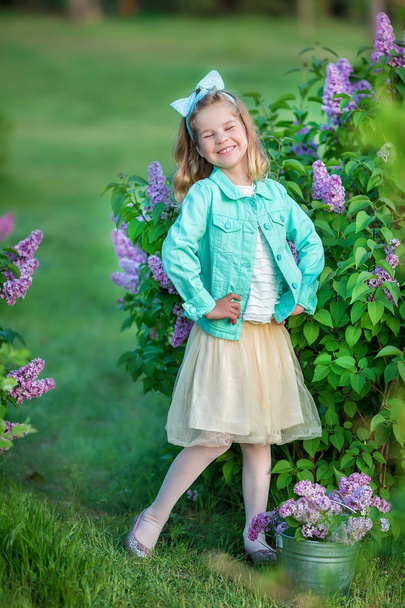 Cute girl in blue jackets with fairy airy skirt standing close to lilac bush - Foto, afbeelding