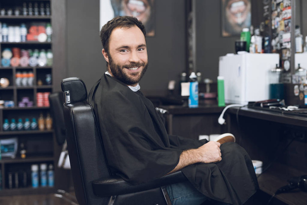 A man sits in a barber's chair in a man's barbershop, where he came to cut his hair. - Zdjęcie, obraz