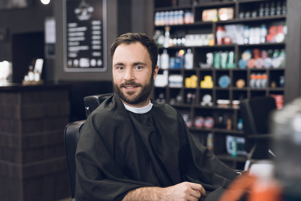 A man sits in a barber's chair in a man's barbershop, where he came to cut his hair. - Foto, Bild