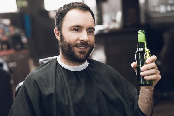 A man drinks alcohol in the hairdresser's armchair of a modern barbershop. - Foto, imagen