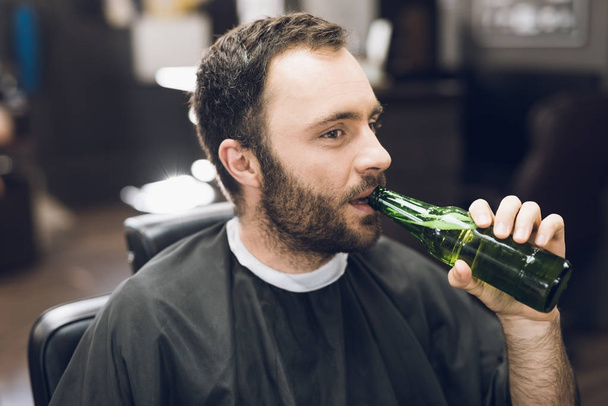 A man drinks alcohol in the hairdresser's armchair of a modern barbershop. - Foto, immagini