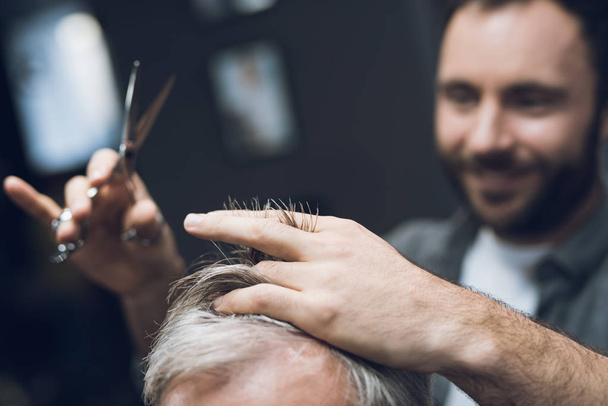 The hairdresser does a hairstyle to an old man with gray hair in a barbershop. - Foto, immagini
