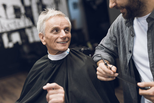 The hairdresser does a hairstyle to an old man with gray hair in a barbershop. - Foto, Bild