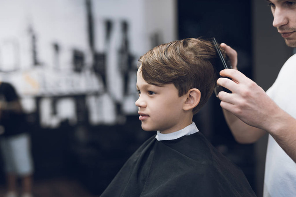 The hairdresser makes a fashionable pretty hairstyle for the boy in a modern barbershop. - Fotoğraf, Görsel