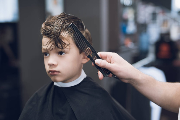 The hairdresser makes a fashionable pretty hairstyle for the boy in a modern barbershop. - Foto, immagini