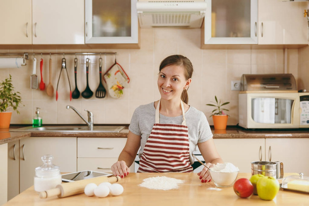 A young beautiful happy woman prepares dough for Christmas cakes with tablet on table in the kitchen. Cooking home. Prepare food. - Фото, изображение