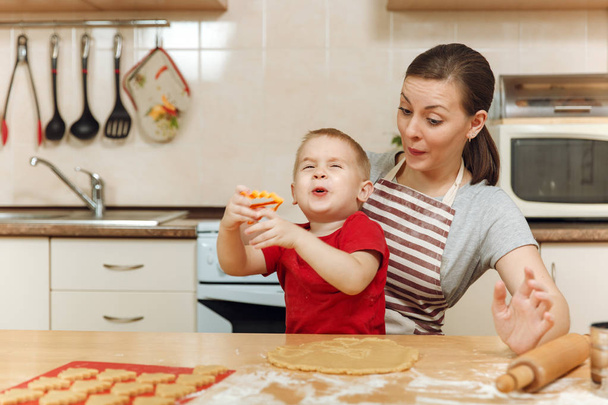 Little kid boy helps mother to cook Christmas ginger biscuit in light kitchen. Happy family mom 30-35 years and child 2-3 roll out dough and cut out cookies at home. Relationship and love concept - Foto, Bild