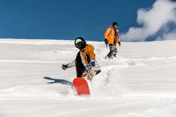 Two snowboarders in sportswear riding down the mountain slope - Fotó, kép