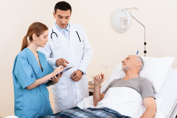 Stary człowiek leży na łóżeczku w oddziale medycznym. Obok niego jest lekarzem i pielęgniarką. - Zdjęcie, obraz