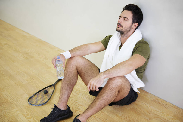 Agotado joven jugador de squash masculino descansando en el suelo
  - Foto, Imagen