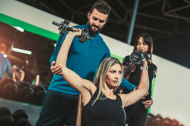 personal trainer helping woman at her workout with heavy dumbbells - Photo, Image