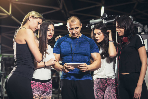 hezký osobní trenér pomocí digitálního tablet, skupina sportovní žen kolem sebe v tělocvičně  - Fotografie, Obrázek