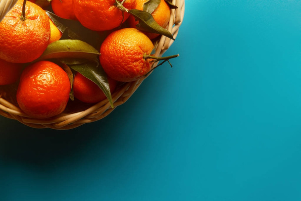 organic ripe mandarins in basket on blue background..tangerines with leaves in a beautiful basket - Photo, image